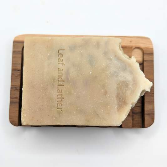 Bar of soap on a wooden soap dish with 'Leaf and Lather' branding on a white background