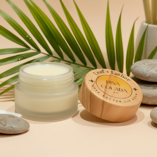 Cosmetic jar, wooden container, and stones on a beige surface with green leaves in the background