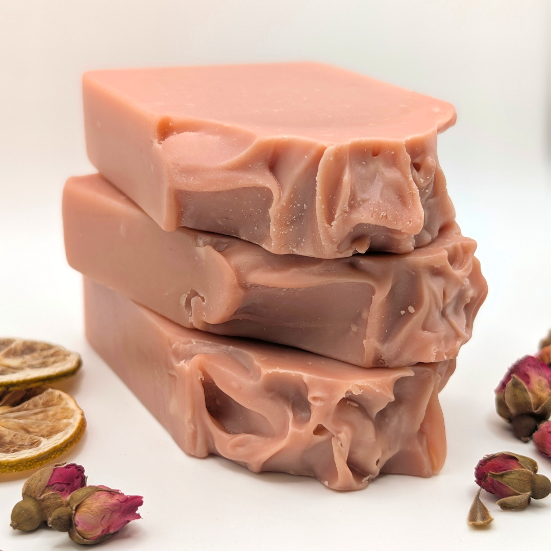 Stack of pink soap bars with dried flowers and leaves on a white background