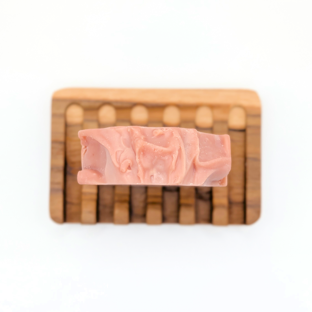 Pink soap bar on a wooden soap dish with a white background