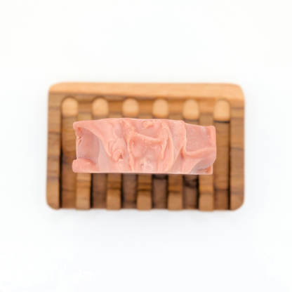 Pink soap bar on a wooden soap dish with a white background