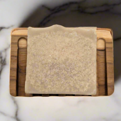 Wooden soap dish with a bar of soap on a marble surface