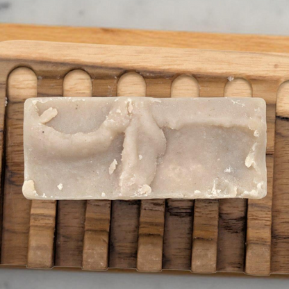 Rectangular soap bar with a wooden soap dish on a marble surface with coffee beans.