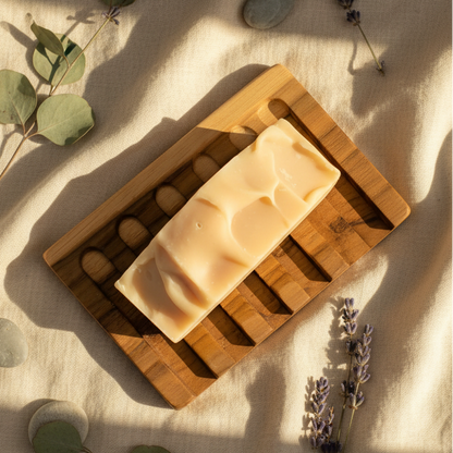 Bar of soap on a wooden soap dish with herbs and stones on a light background
