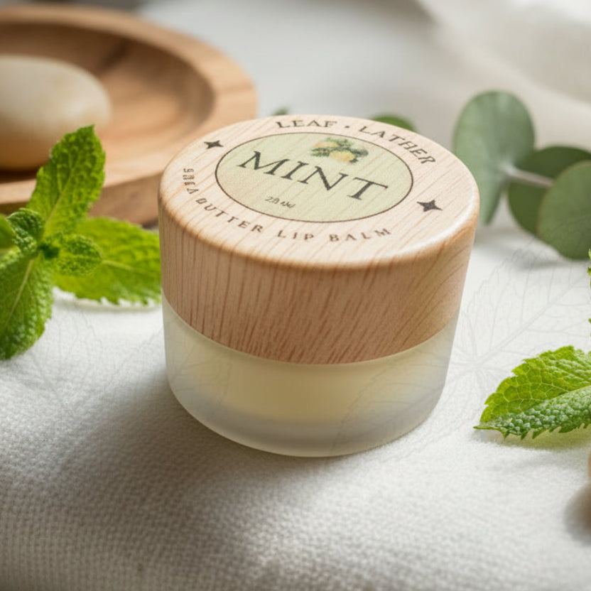 Lip balm with a wooden cap labeled 'Mint' on a white cloth with mint leaves.