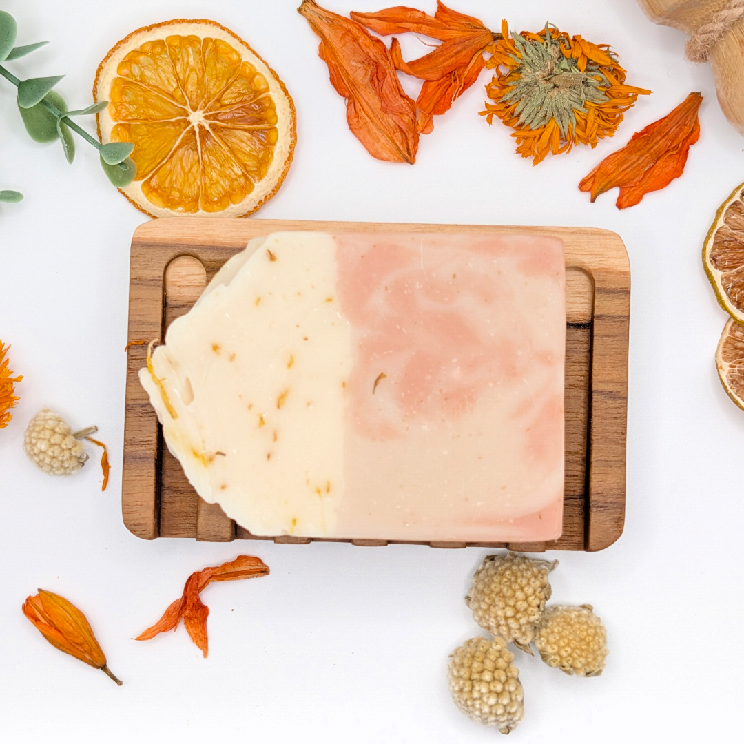 Two layered soap bar on a wooden board with dried orange slices and flowers on a white background