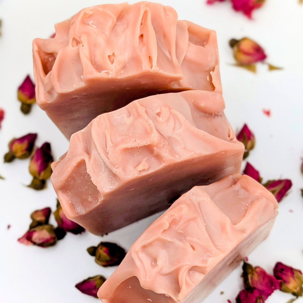 Three bars of pink soap with a decorative pattern on a white background with dried roses.