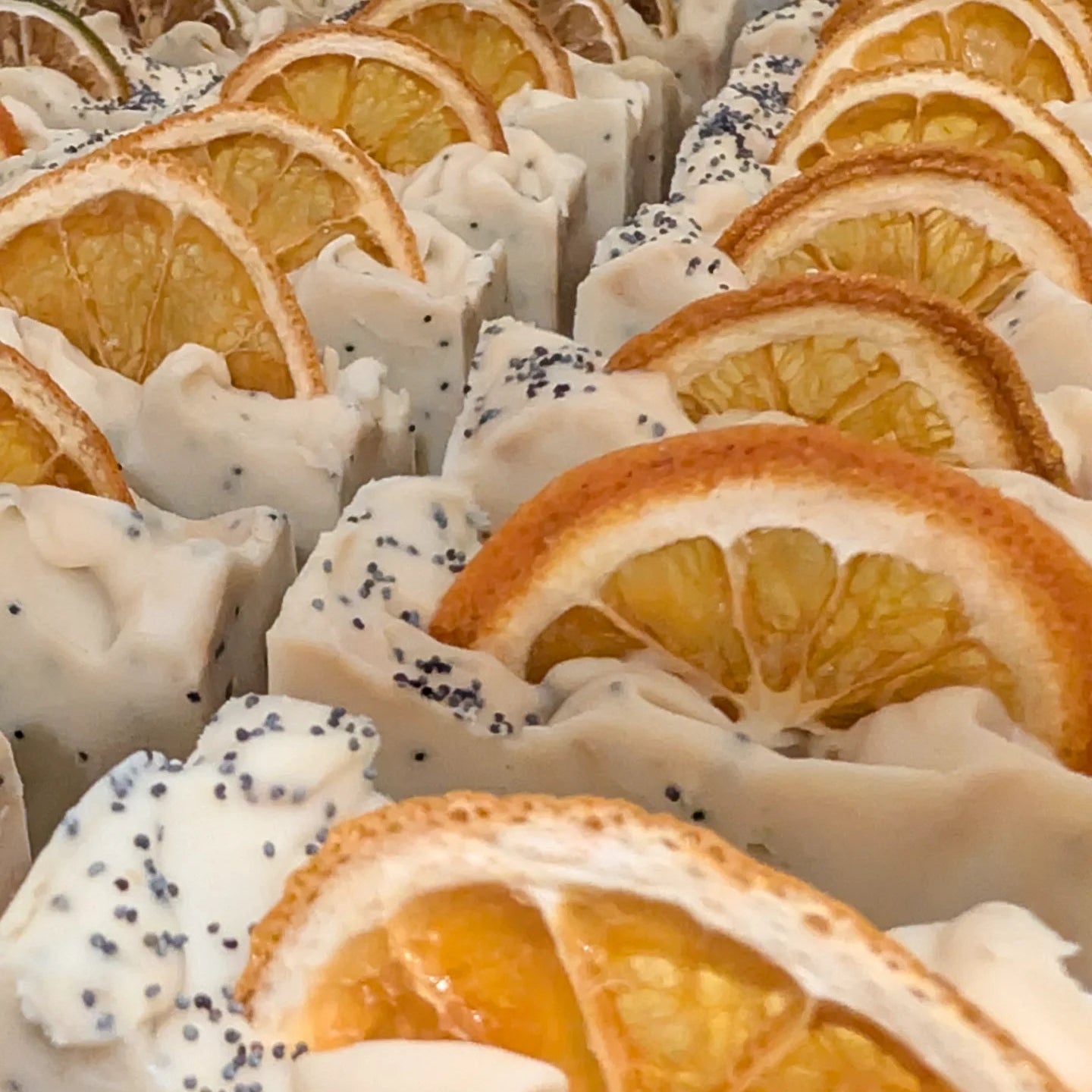 Row of soap bars with orange slices and poppy seeds on a white background