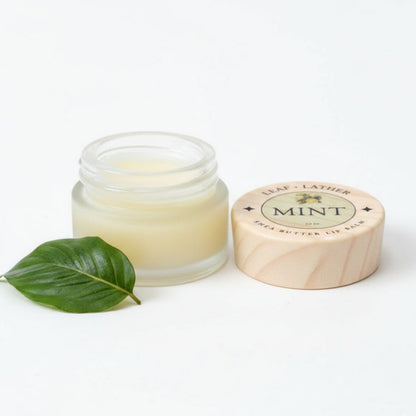 Jar of lip balm with a wooden lid and green leaf on a white background