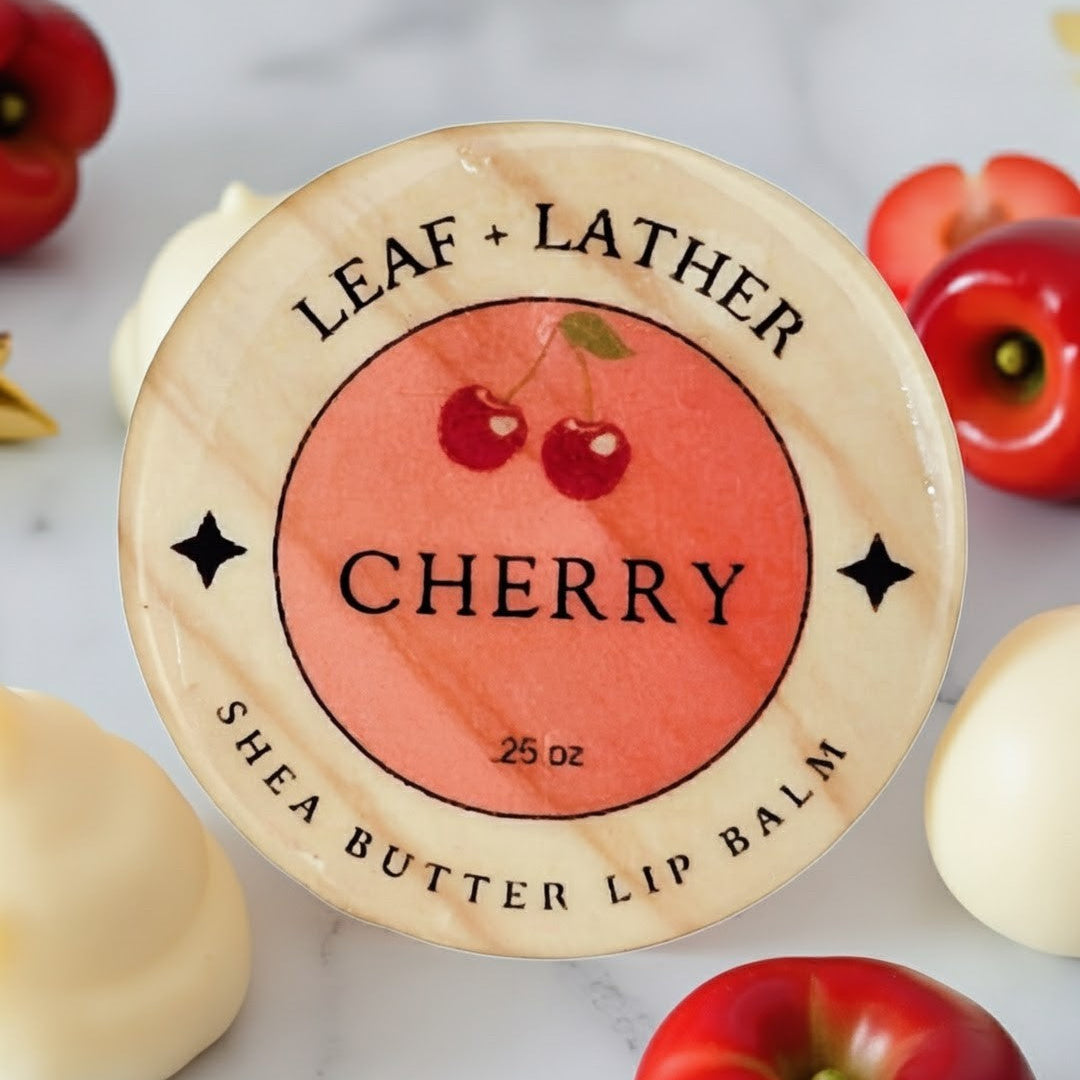 Shea butter lip balm with cherry design and 'Leaf + Lather' branding on a marble surface.