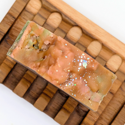 Bar of soap with glitter on a wooden soap dish against a white background