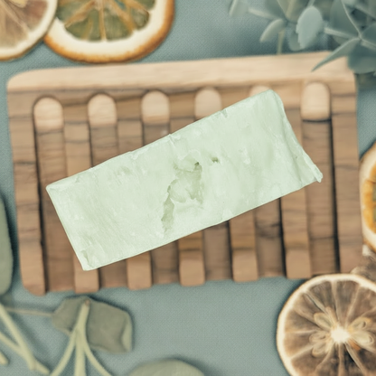 Green bar of soap on a wooden cutting board with dried oranges and leaves on a teal background