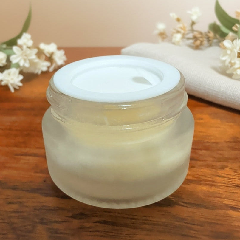Frosted glass jar with a white lid on a wooden surface with flowers in the background