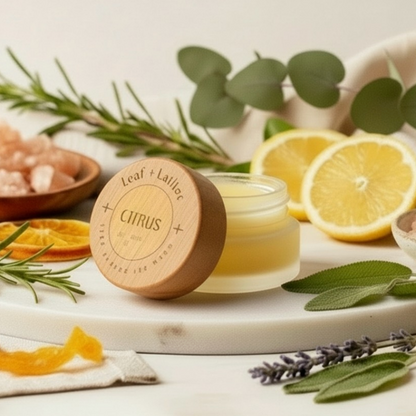 Jar of citrus product with natural elements like lemons, lavender, and rosemary on a light background