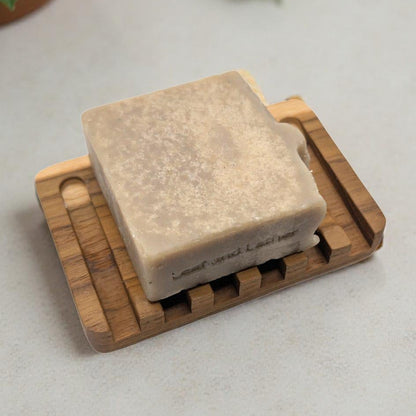 Square bar of soap on a wooden soap dish with plants and berries on a light surface