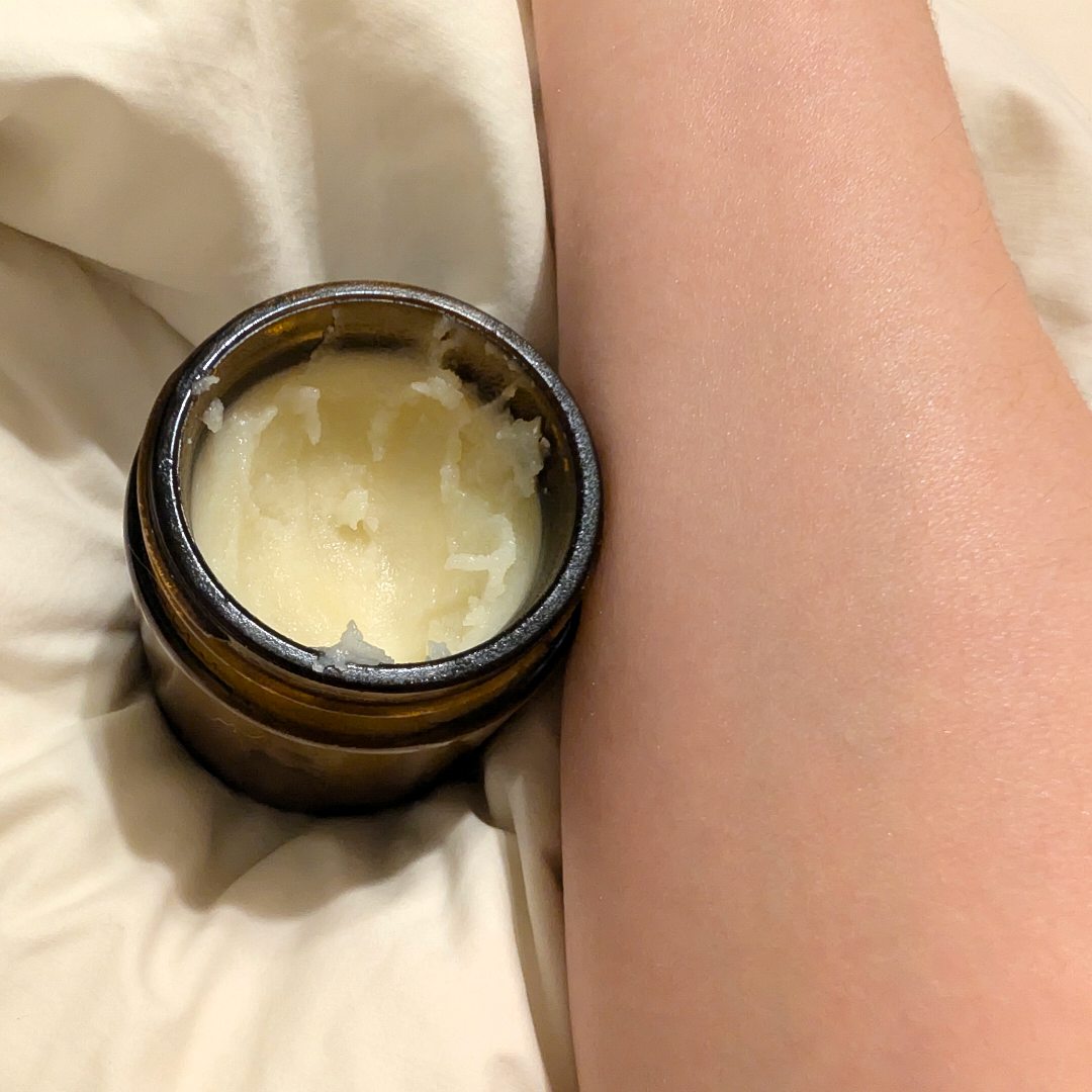 Small container of cream on a person's wrist against a neutral background