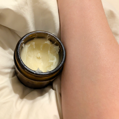 Small container of cream on a person's wrist against a neutral background