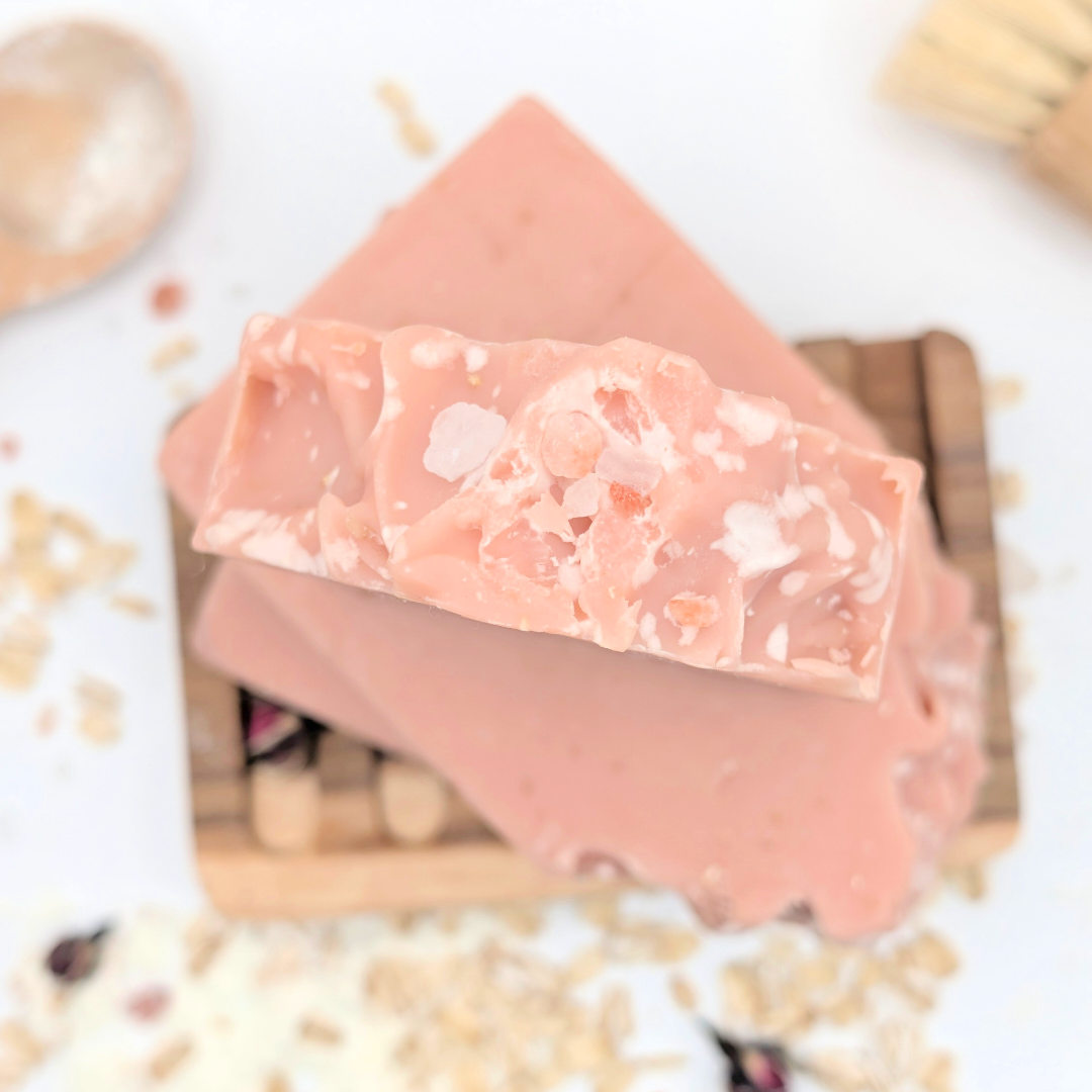 Pink soap bar with visible specks on a wooden block with a light background