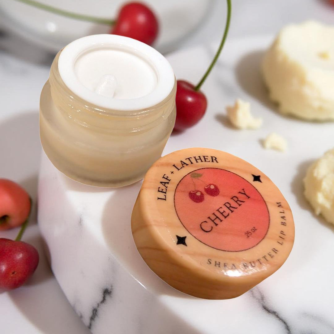 Jar of shea butter lip balm with cherry flavor on a marble surface with cherries around
