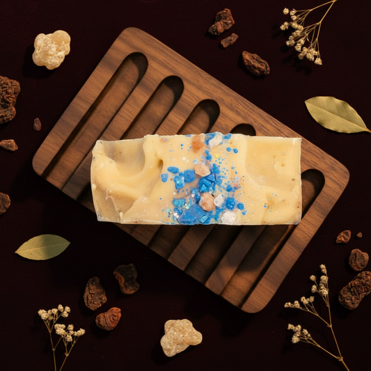 Bar of soap with blue specks on a wooden soap dish against a blue background