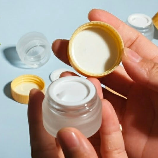 Person holding a small clear container with a yellow lid against a light blue background