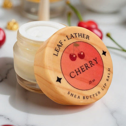 Jar of cherry-scented shea butter lip balm with wooden lid on a marble surface.