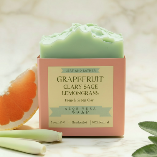 Grapefruit Clary Sage Lemongrass soap bar with packaging on a wooden stand, surrounded by fresh ingredients.